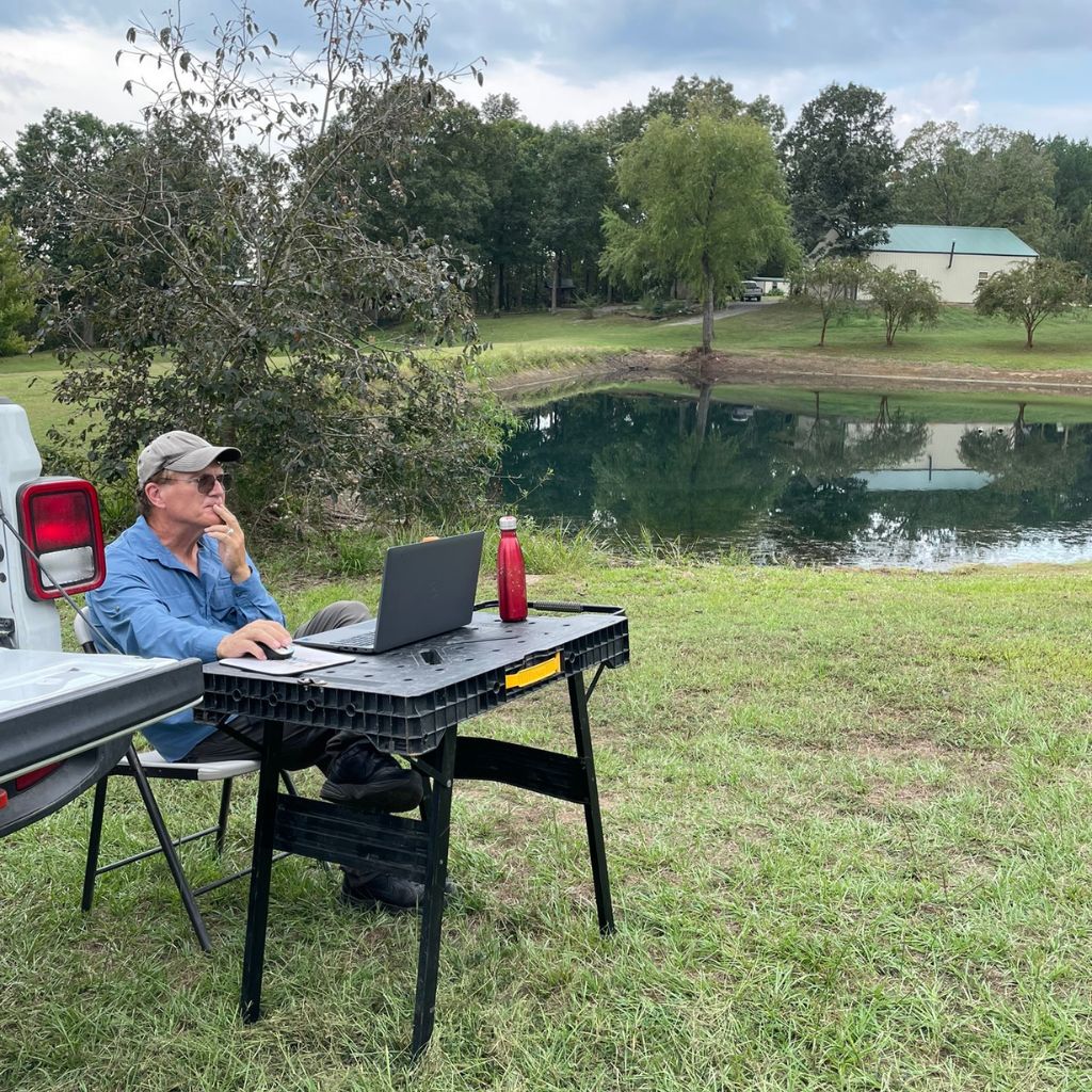 Andrew Vandekop of Well Water Finders reviewing groundwater survey results on-site with a laptop near an Arkansas pond, providing immediate land and water decision support.